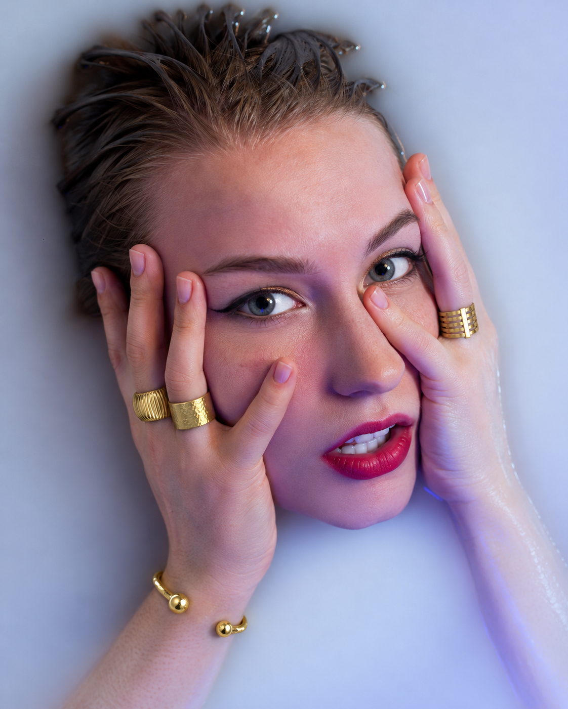 Gold rings and a gold cuff worn in a close-up portrait