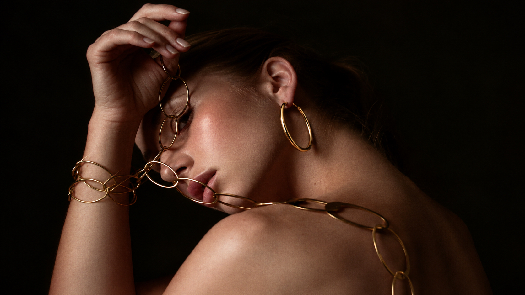 Gold hoops and linked jewelry in a dramatic portrait